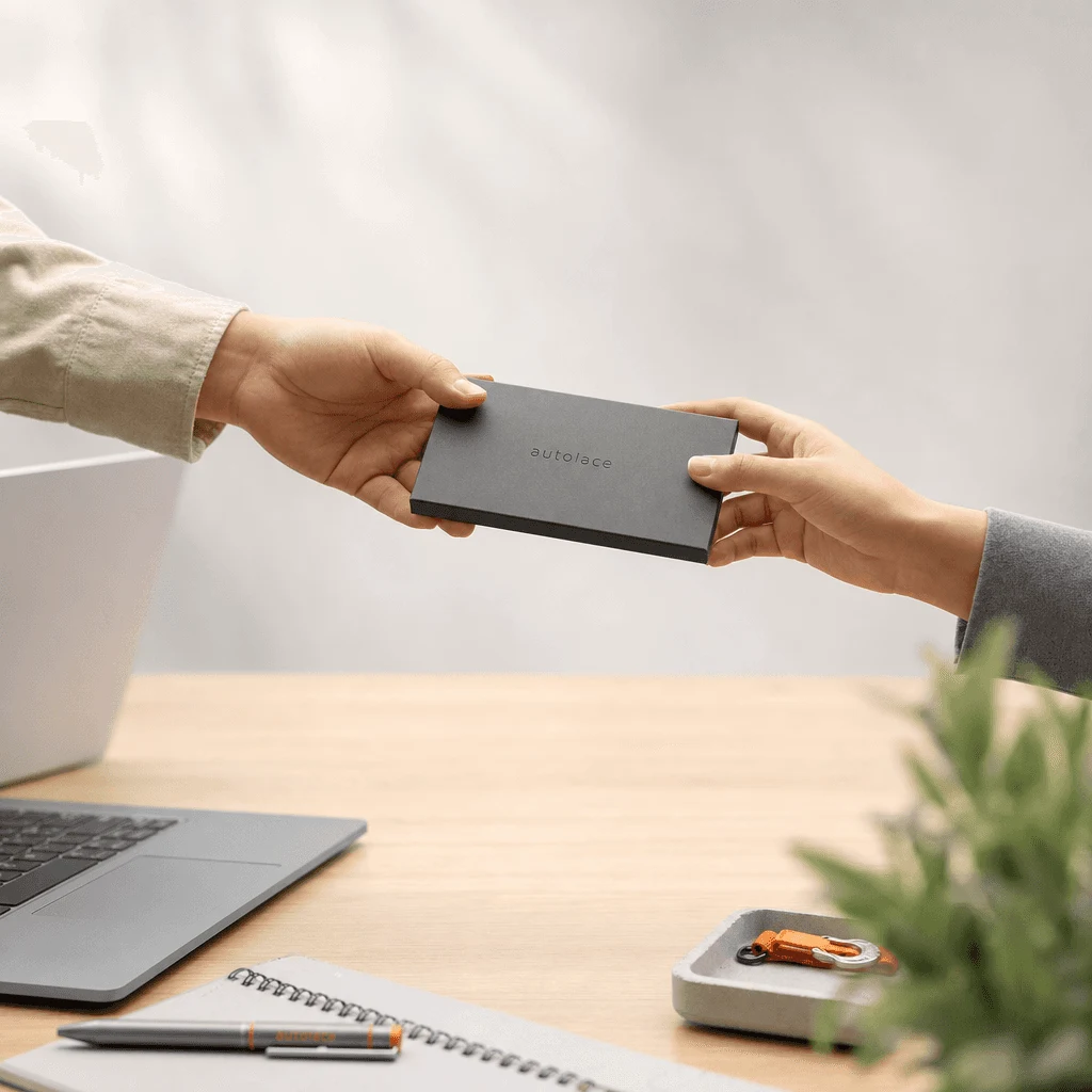 Two hands exchanging an engraved Autolace box over a desk